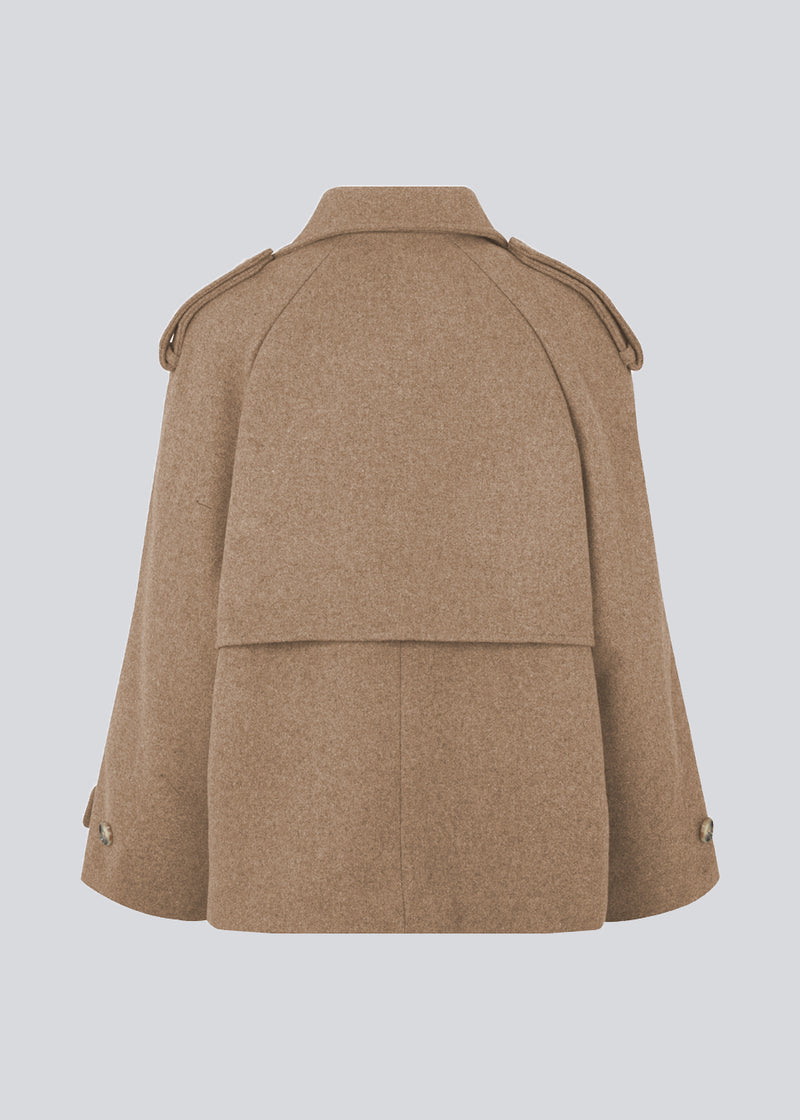 Cropped dobbeltradet uldfrakke med skjulte knapper. EsmundMD jacket i fraven Brown Sugar har klassiske frakkedetaljer med raglanærmer og bredt bærestykke på ryggen. Med foer. Modellen er 175 cm og har en størrelse S/36 på.
