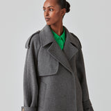 Cropped dobbeltradet uldfrakke med skjulte knapper. EsmundMD jacket i farven Dark Grey Melange har klassiske frakkedetaljer med raglanærmer og bredt bærestykke på ryggen. Med foer. Modellen er 175 cm og har en størrelse S/36 på.
