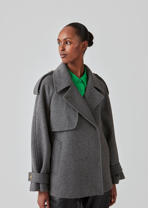 Cropped dobbeltradet uldfrakke med skjulte knapper. EsmundMD jacket i farven Dark Grey Melange har klassiske frakkedetaljer med raglanærmer og bredt bærestykke på ryggen. Med foer. Modellen er 175 cm og har en størrelse S/36 på.