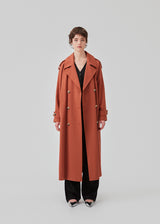 Oversized dobbeltradet trench coat i farven Maple med bindebånd i taljen. EvieMD jacket har lav skuldersøm og lange, brede ærmer. Med foer. Modellen er 175 cm og har en størrelse S/36 på.