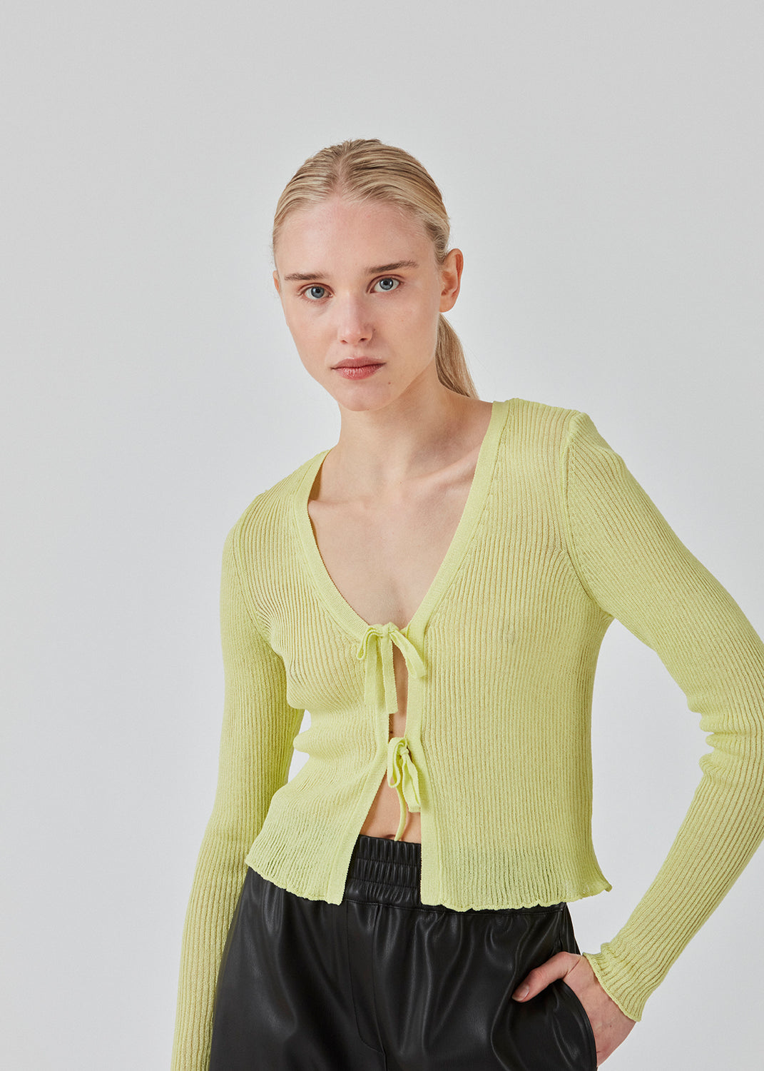 Tyndt strikket cardigan i farven Limonade med let gennemsigtigt udtryk. FaddieMD cardigan er let cropped, har lange ærmer og lukkes med bindebånd fortil. Modellen er 175 cm og har en størrelse S/36 på.