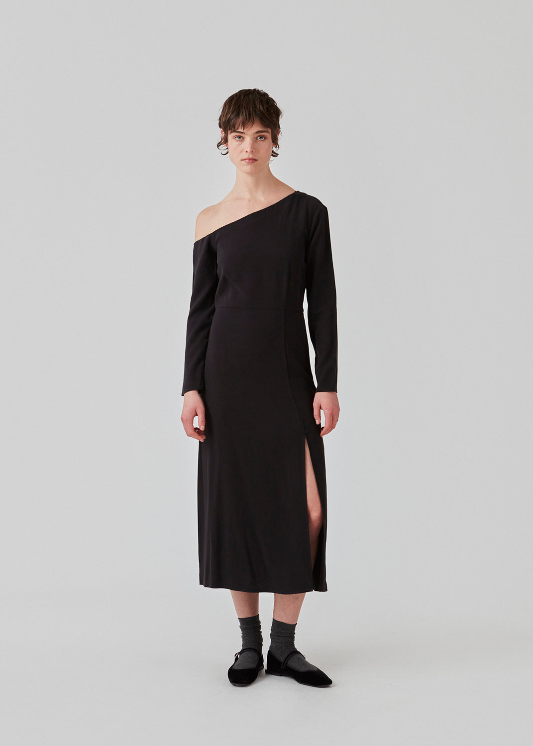 Midi-kjole designet i kvalitet af EcoVero viskose. FanyaMD long dress har en normal facon med asymmetriske, lange ærmer med bar skulder, skæring i taljen og slids foran. Modellen er 175 cm og har en størrelse S/36 på.