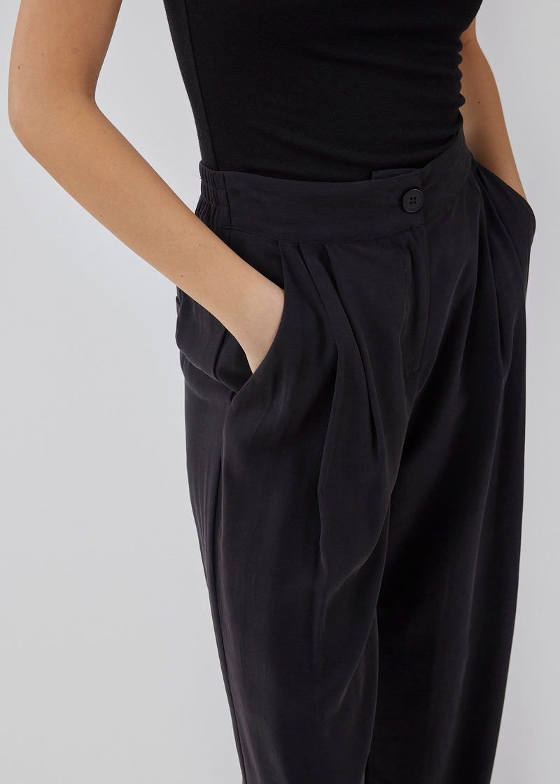 FanyaMD pants i sort har et herre-inspireret look med lige, brede ben, høj talje med lynlåsgylp og knap og elastik bagpå. Dobbeltlæg fo