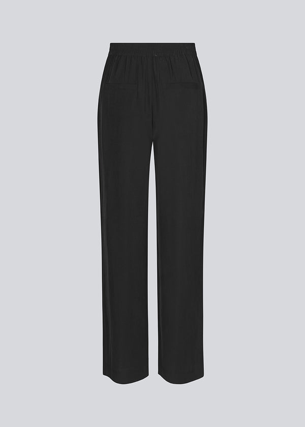 FanyaMD pants i sort har et herre-inspireret look med lige, brede ben, høj talje med lynlåsgylp og knap og elastik bagpå. Dobbeltlæg foran og sidelommer. 