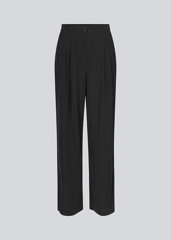 FanyaMD pants i sort har et herre-inspireret look med lige, brede ben, høj talje med lynlåsgylp og knap og elastik bagpå. Dobbeltlæg foran og sidelommer. '