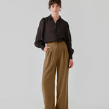 FanyaMD pants i brun har et herre-inspireret look med lige, brede ben, høj talje med lynlåsgylp og knap og elastik bagpå. Dobbeltlæg foran og sidelommer. Modellen er 175 cm og har en størrelse S/36 på.