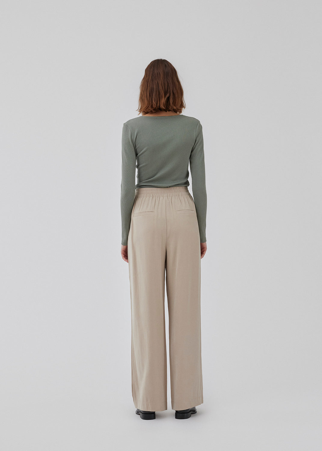 FanyaMD pants i lys beige har et herre-inspireret look med lige, brede ben, høj talje med lynlåsgylp og knap og elastik bagpå. Dobbeltlæg foran og sidelommer. Modellen er 175 cm og har en størrelse S/36 på.