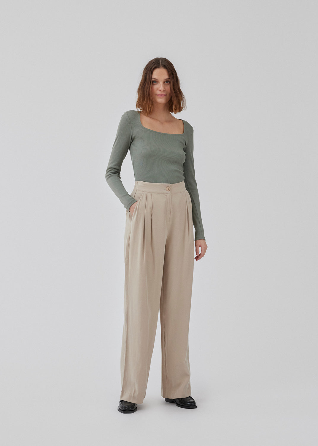 FanyaMD pants i lys beige har et herre-inspireret look med lige, brede ben, høj talje med lynlåsgylp og knap og elastik bagpå. Dobbeltlæg foran og sidelommer. Modellen er 175 cm og har en størrelse S/36 på.