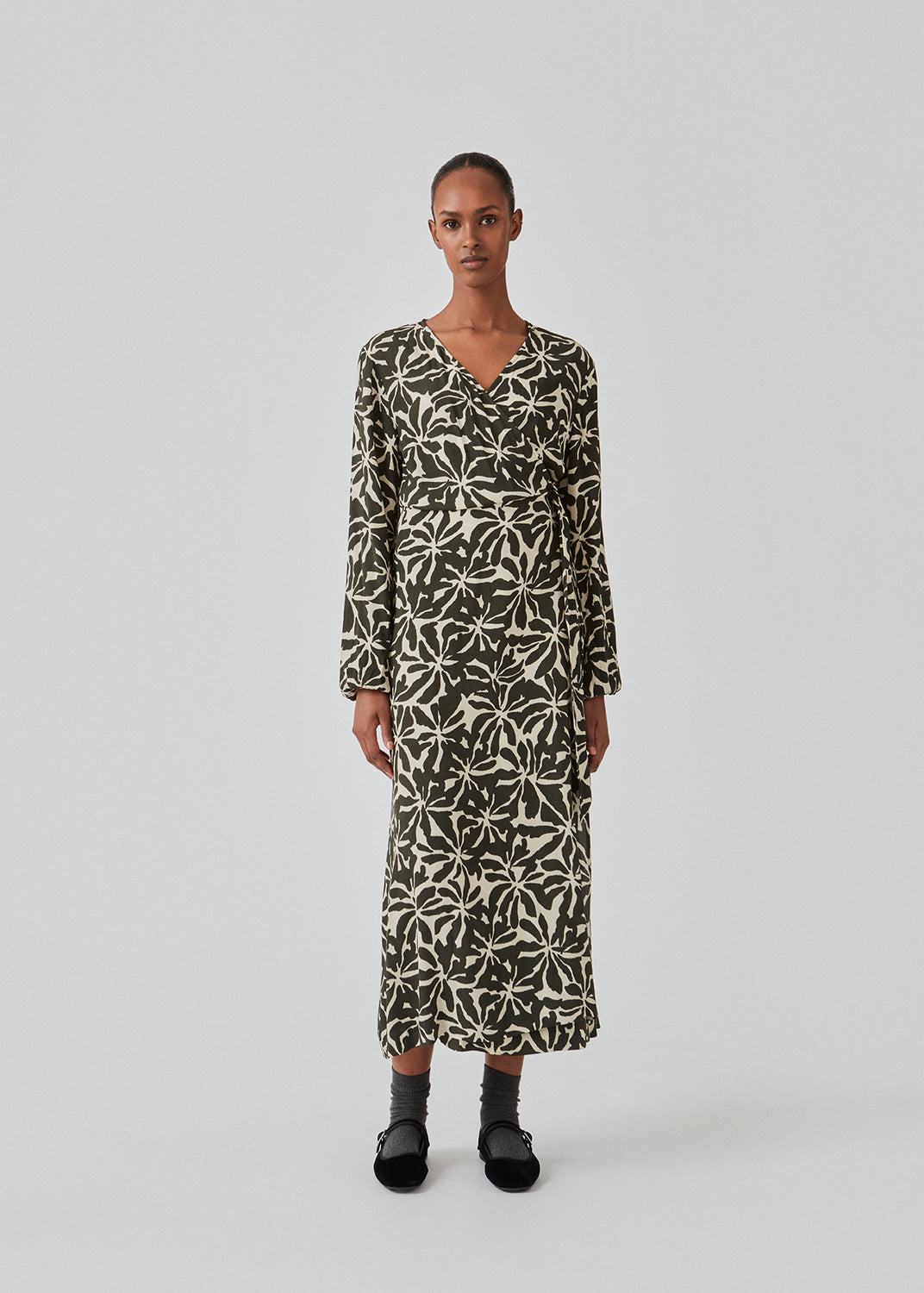 Midi-kjole i printet EcoVero viskose med v-udskæring og wrap-effekt foran. FernMD print wrap dress har bredt bindebælte i taljen og lange ballonærmer. Modellen er 175 cm og har en størrelse S/36 på.