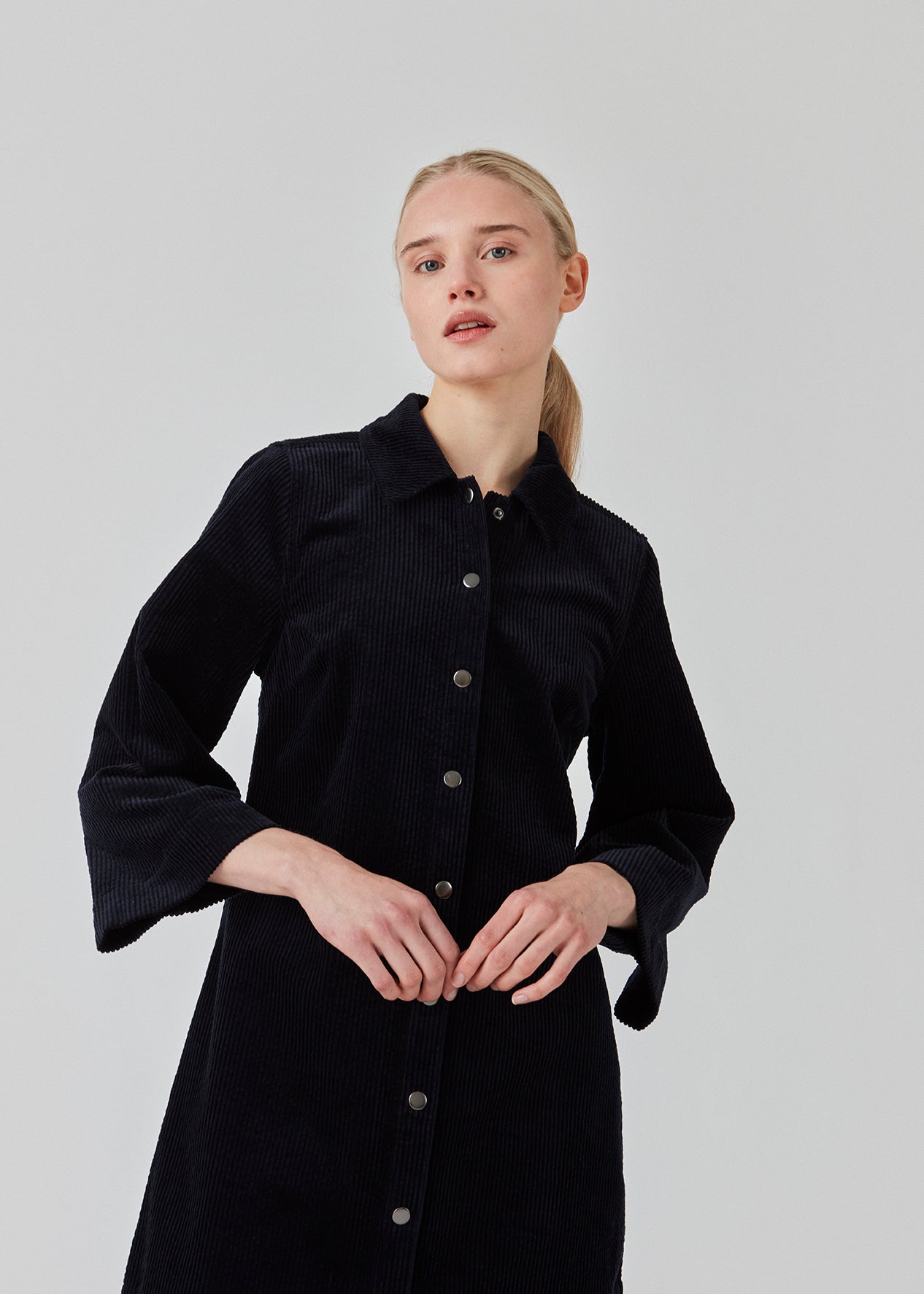 Midi skjortekjole i fløjl i mørkeblå med krave og trykknapper foran. FikaMD dress har et rummeligt fit med A-silhuet og 3/4 lange brede ærmer. Modellen er 175 cm og har en størrelse S/36 på.