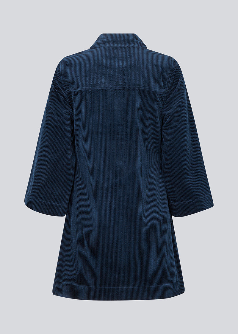Midi skjortekjole i fløjl i mørkeblå med krave og trykknapper foran. FikaMD dress har et rummeligt fit med A-silhuet og 3/4 lange brede ærmer. Modellen er 175 cm og har en størrelse S/36 på.