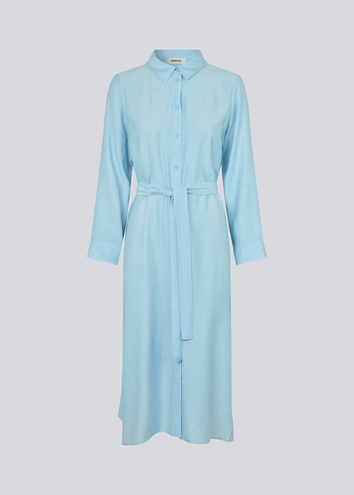 Midi-kjole i lyseblå i vævet kvalitet med krave, knapper foran, aftageligt bindebælte i taljen og slidser i siden. Lange ærmer med manchet. Modellen er 175 cm og har en størrelse S/36 på.