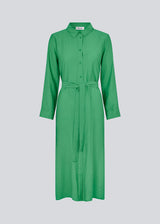 Midi-kjole i grøn i vævet kvalitet med krave, knapper foran, aftageligt bindebælte i taljen og slidser i siden. Lange ærmer med manchet. Modellen er 175 cm og har en størrelse S/36 på.