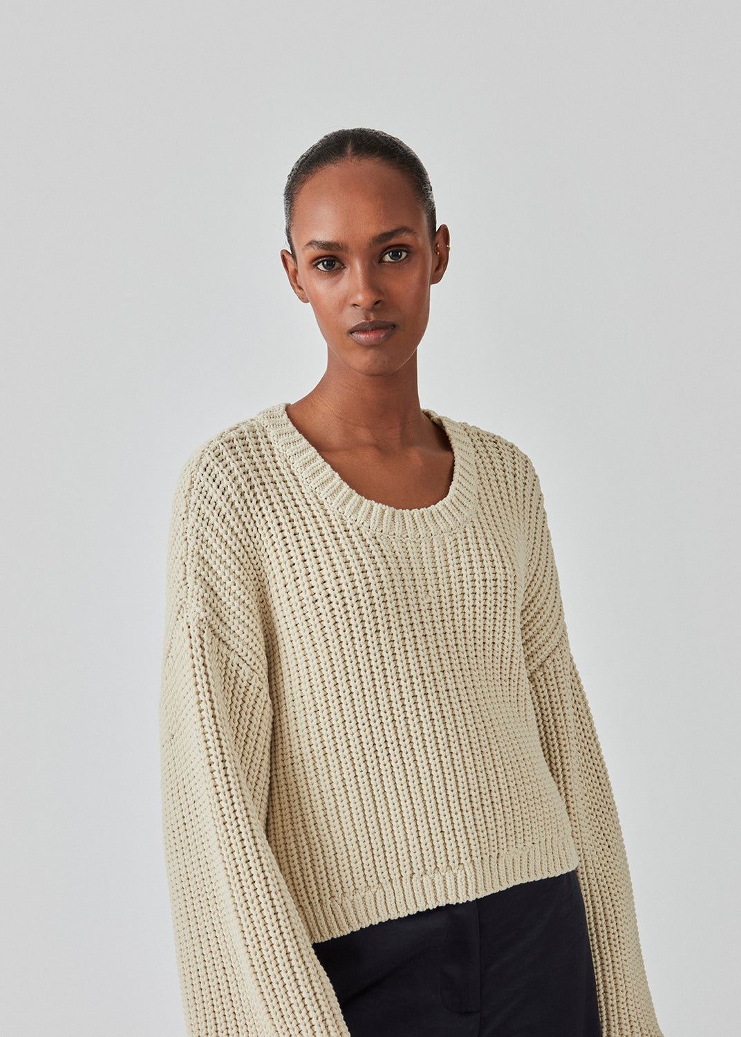 Grovstrikket trøje i beige i bomuldsstrik med bred, rund hals og let cropped længde. FlakaMD o-neck har en afslappet silhuet med ekstra lange ballonærmer. Modellen er 175 cm og har en størrelse S/36 på.