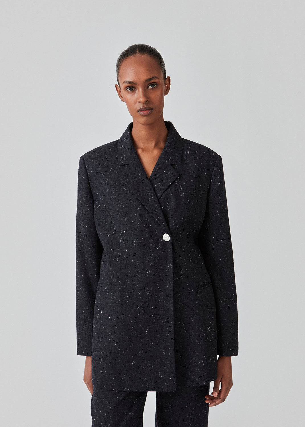 Oversized dobbeltradet blazer med en enkelt synlig knap. FolaMD blazer er lavet i materiale med uld og små farvede nister. Del af sæt, køb bukserne her: FolaMD. Modellen er 175 cm og har en størrelse S/36 på.