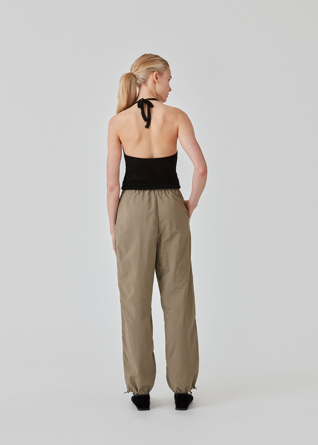 Faldskærmsbukser i beige i nylon med afslappet pasform. FumikoMD pants har almindelig talje med elastik, vide ben og elastisk snøre forneden. Modellen er 175 cm og har en størrelse S/36 på.