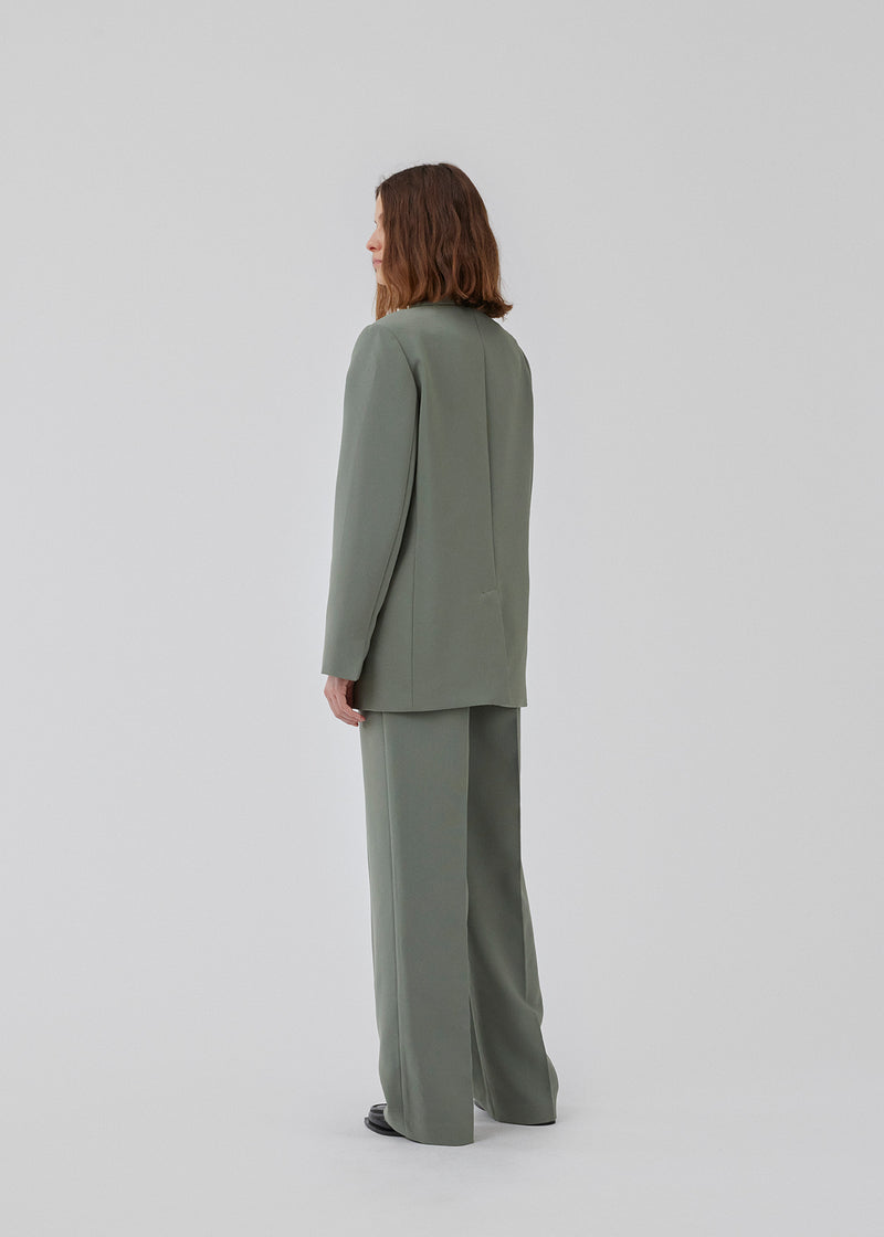 Gale blazer i sart grøn har et klassisk og elegant design, som kommer til udtryk i den flotte reverskrave og den lange pasform. Blazeren har knaplukning fortil og en brystlomme i venstre side. Modellen er 175 cm og har en størrelse S/36 på.
