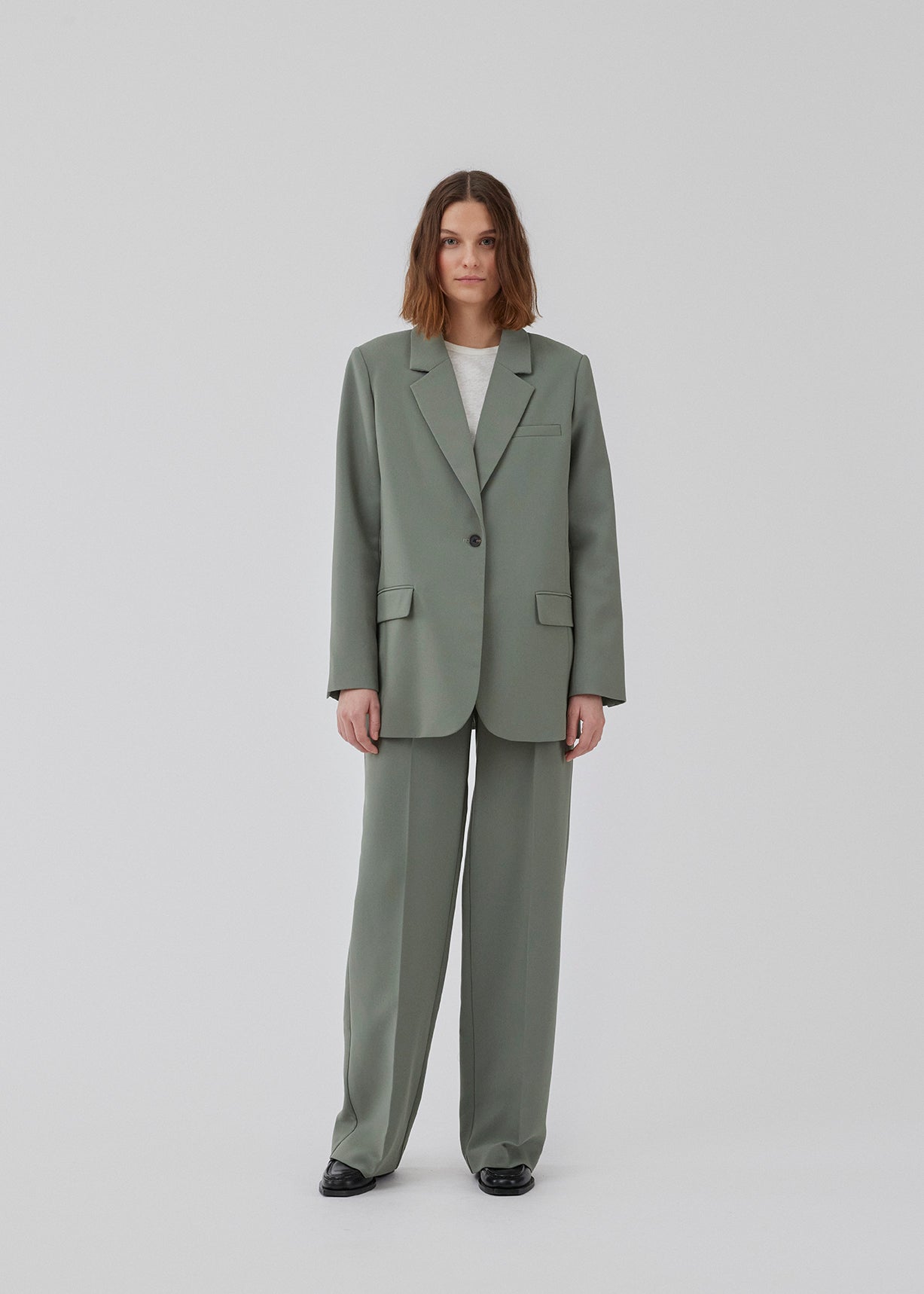 Gale pants i grøn har et klassisk design. Buksen har lige, vide ben med pressefolder som skaber et elegant udtryk. Modellen er 175 cm og har en størrelse S/36 på. Indersøm (S/36): 83 cm Bukserne forlænges med 0,5 cm for hver størrelse.