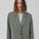 Gale blazer i sart grøn har et klassisk og elegant design, som kommer til udtryk i den flotte reverskrave og den lange pasform. Blazeren har knaplukning fortil og en brystlomme i venstre side. Modellen er 175 cm og har en størrelse S/36 på.