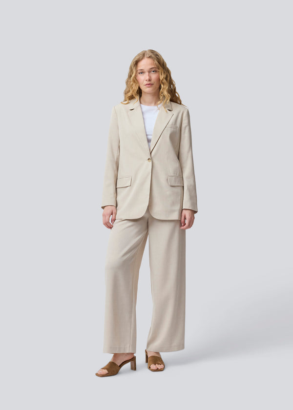 GaleMD 2 blazer i beige melange har det klassiske og velkendte Gale-design, men i en lettere kvalitet. Blazeren har knaplukning fortil og en brystlomme i venstre side. Modellen er 175 cm og har en størrelse S/36 på.