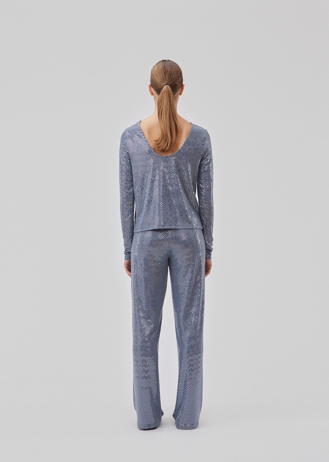 GiaMD top har en smal silhuet med rund hals og lange ærmer. Toppen er detaljerert med pailletter og en stor udskæring i ryggen. Modellen er 175 cm og har en størrelse S/36 på.  Shop matchende bukser: GaiMD pants.