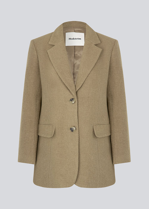 Enkeltradet blazer i strukturvævet kvalitet med uld. GinniMD jacket har et oversize fit med krave og revers, forlommer med klap og slids bagpå. Med foer. Modellen er 175 cm og har en størrelse S/36 på.