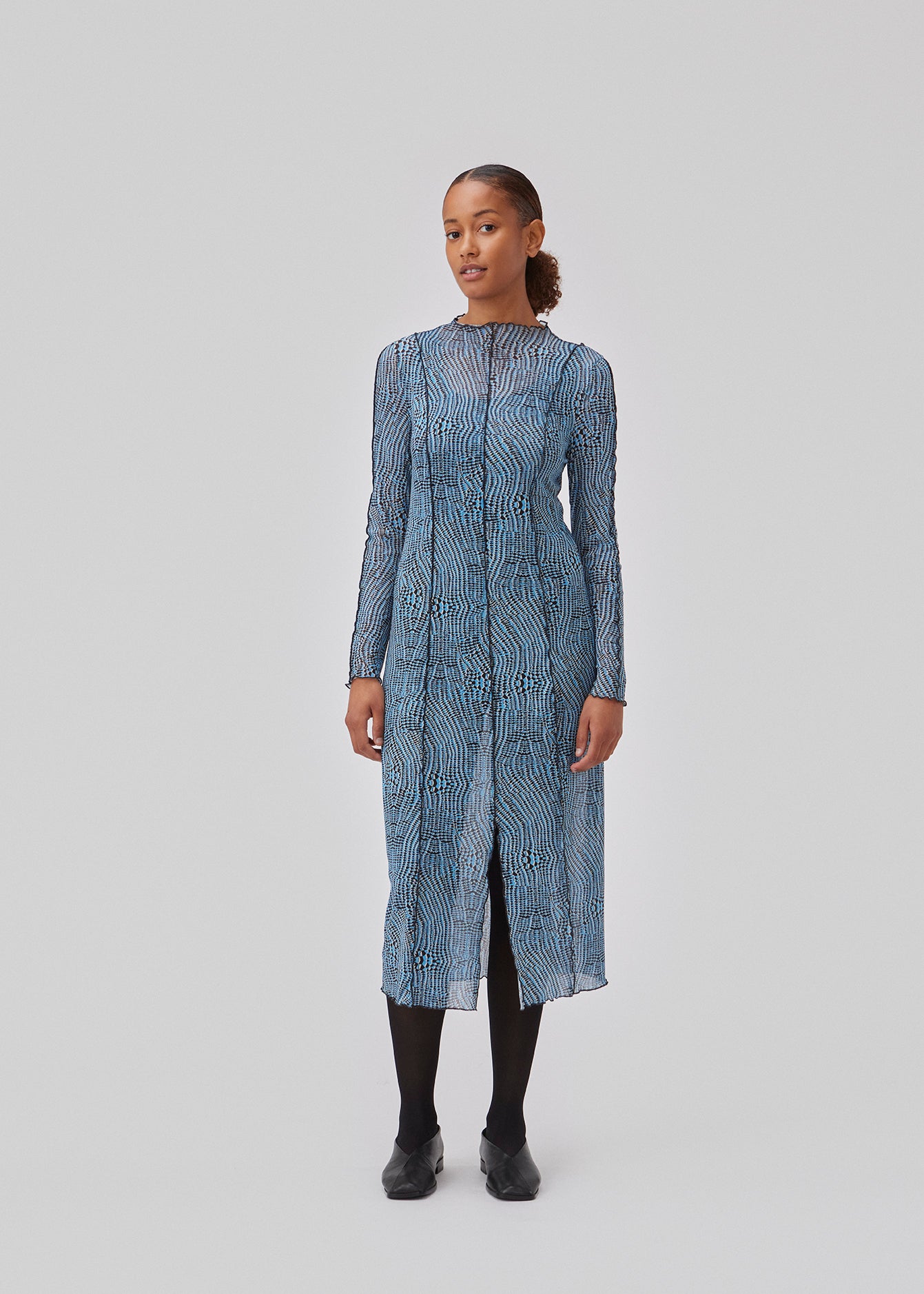 Kjole i mesh med høj hals, lange ærmer og midi længde. GwenMD print dress har dekorative bølgekanter på krop, hals og ærmer. Kjolen har slids foran og er en smule transparent. Modellen er 175 cm og har en størrelse S/36 på.