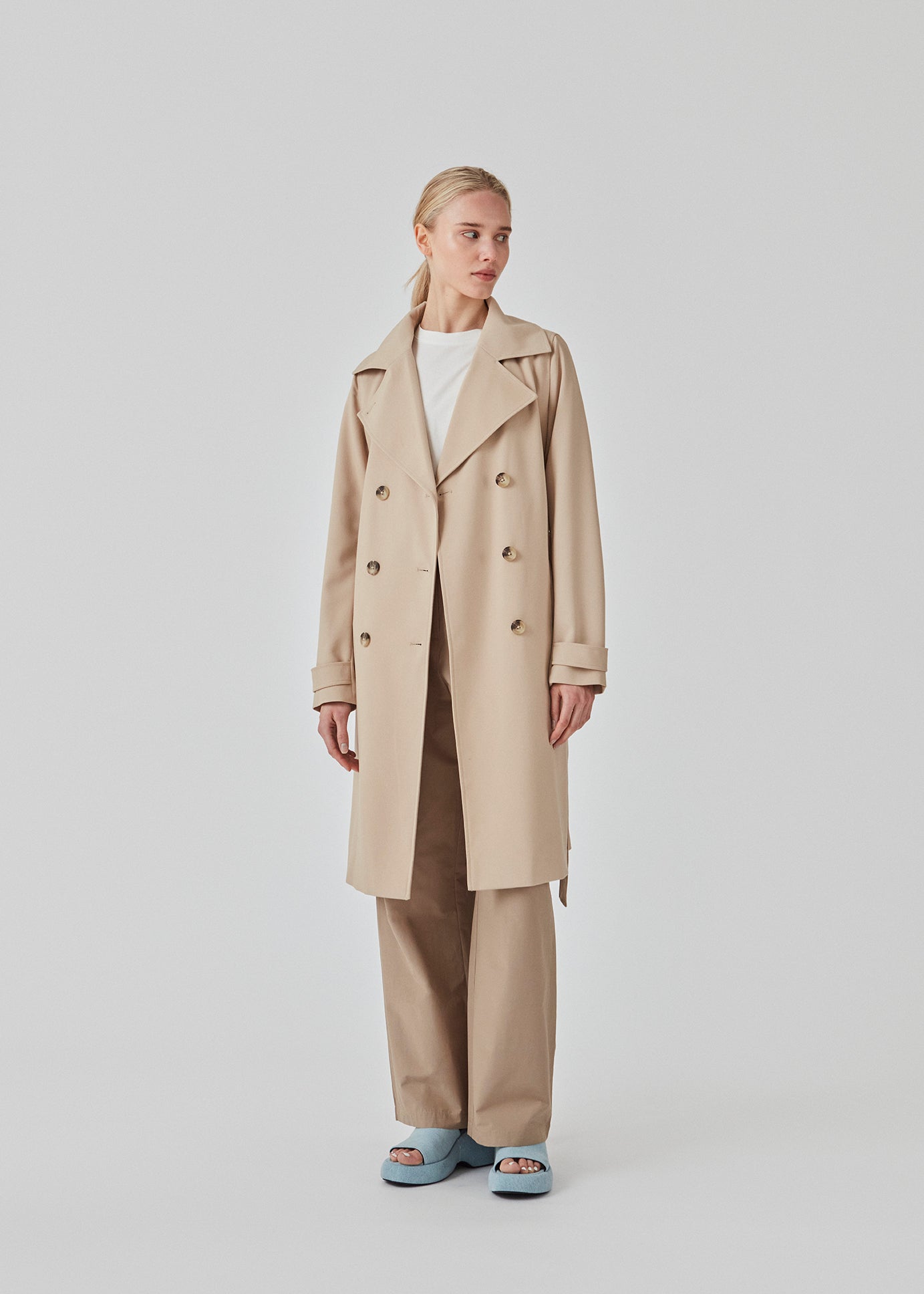 Trenchcoat jakke i beige med i et klassisk udtryk bred krave, bælte i livet og knaplukning. Hiro jacket er perfekt som overgangsjakke fra vinter til forår. Jakken har en rummelig pasform. Vi anbefaler at gå en størrelse ned. Modellen er 174 cm og har en størrelse S/36 på.