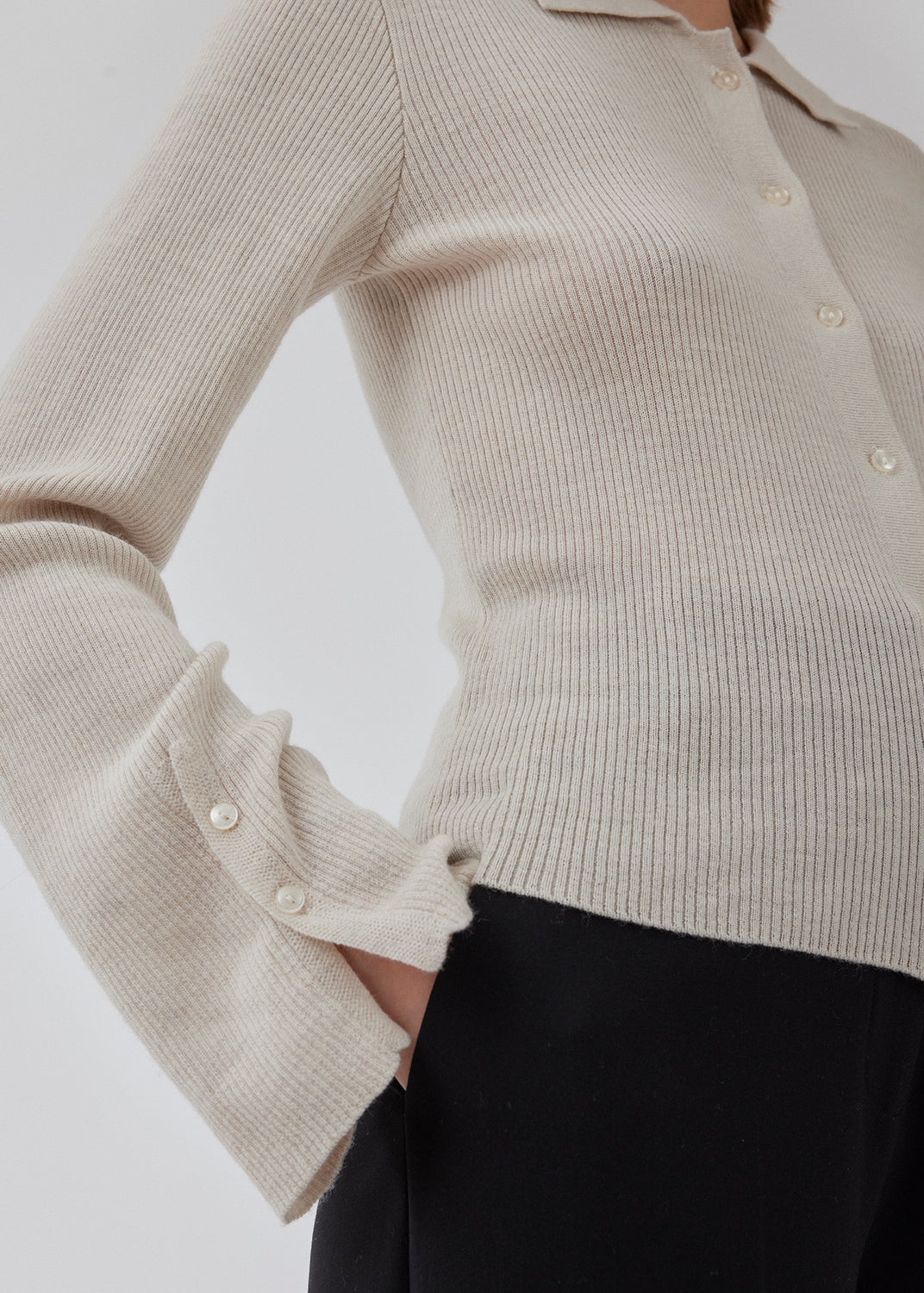 Tætsiddende cardigan io beige i blød ribstrik af uld. HirokiMD cardigan har krave, knapper foran og lange ærmer med slids og knapper. Modellen er 175 cm og har en størrelse S/36 på.
