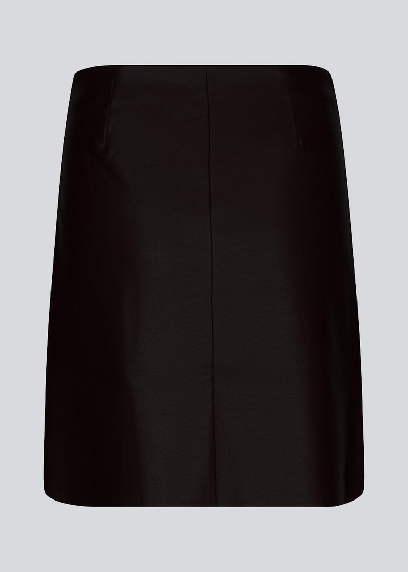 Kort, asymmetrisk slå om-nederdel i sort i imiteret læder. HuxleyMD skirt har en skjult lynlås i den ene side. Modellen er 175 cm og har en størrelse S/36 på.