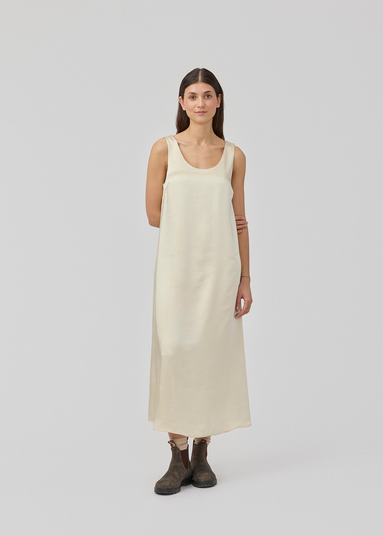 Lang kjole i beige i satin med A-formet silhuet. IolaMD dress har en dyb rygudskæring og brede stropper. Modellen er 177 cm og har en str S/36 på.