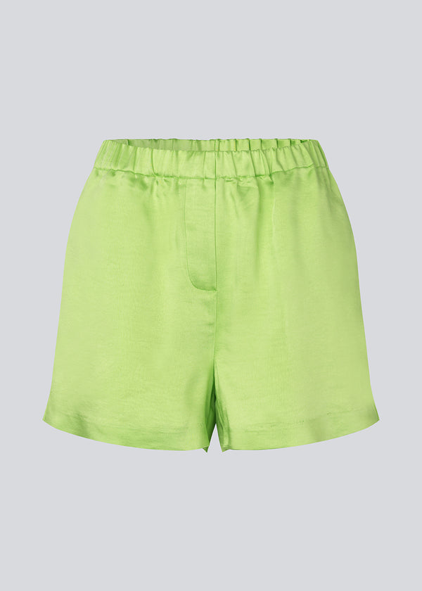 Løse shorts i grøn i satin med elastik i taljen. IolaMD shorts har en mellemhøj taljeog sidelommer. Modellen er 177 cm og har en størrelse S/36 på.