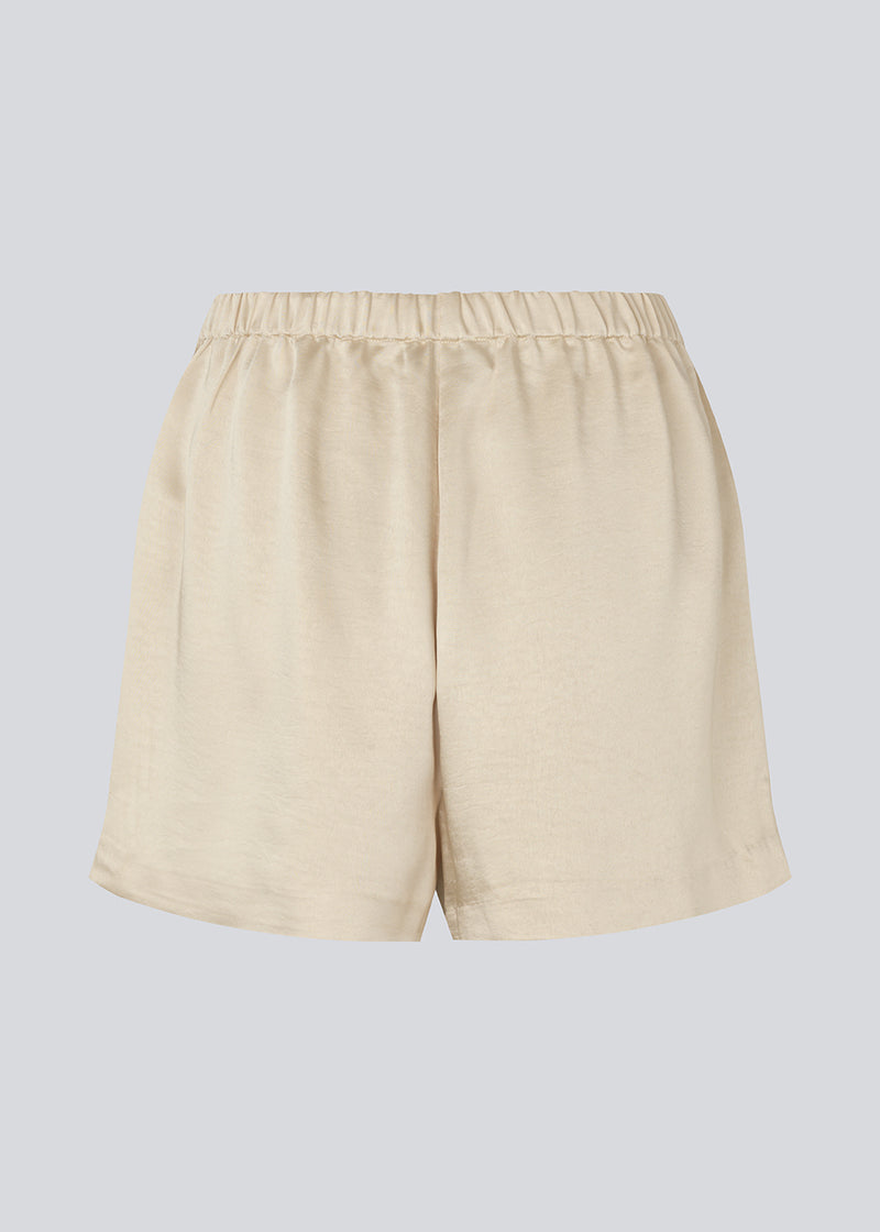 Løse beige shorts i satin med elastik i taljen. IolaMD shorts har en mellemhøj taljeog sidelommer. Modellen er 177 cm og har en størrelse S/36 på.
