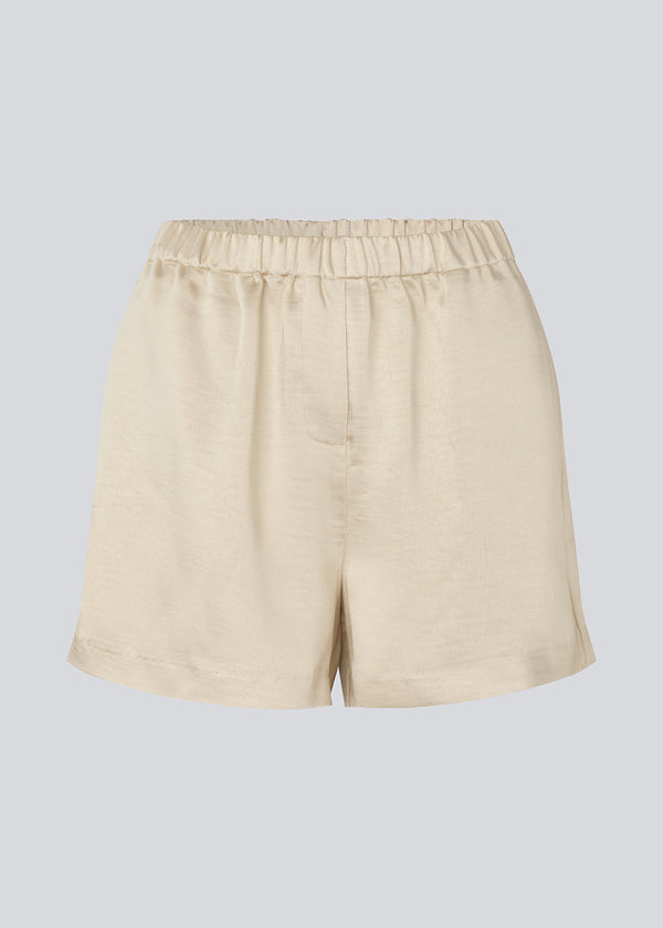 Løse beige shorts i satin med elastik i taljen. IolaMD shorts har en mellemhøj taljeog sidelommer. Modellen er 177 cm og har en størrelse S/36 på.
