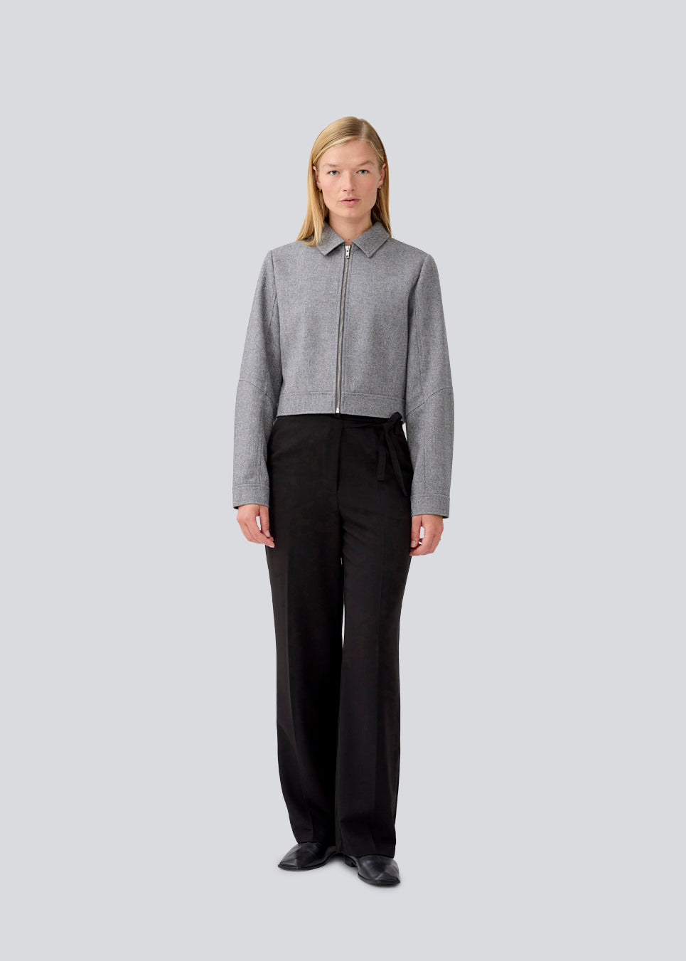 Let cropped jakke i 80% uld. LissieMD jacket er grå, har en klassisk krave, lynlås lukning fortil og manchet med trykknap. Modellen er 177 cm og har en størrelse S/36 på.