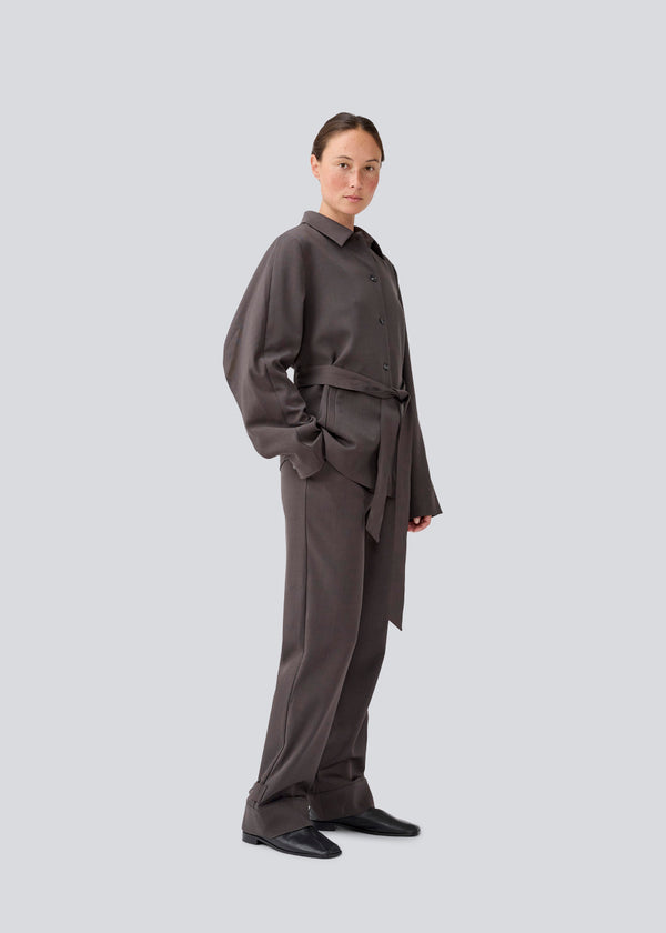 Habitbukser i mørkegrå med spændedetalje. LonnieMD pants har lynlås, sidelommer og elastik i taljen. Modellen er 177 cm og har en størrelse S/36 på.