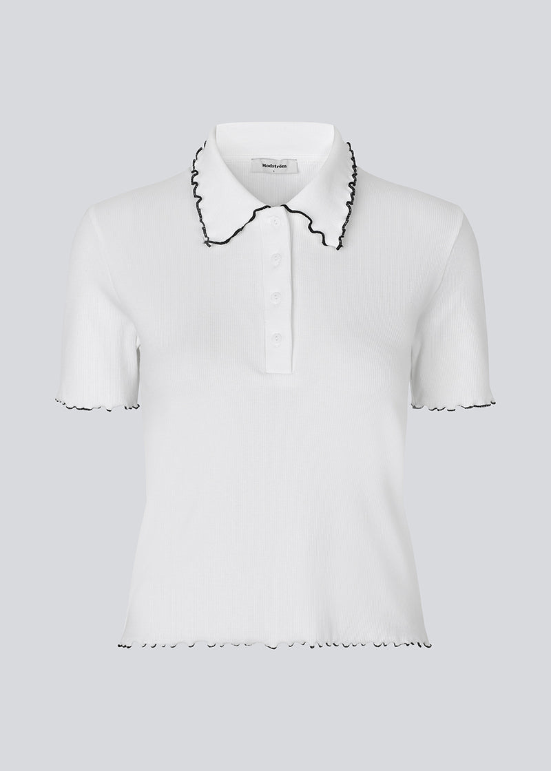 Figursyet polo t-shirt i hvid med sorte kanter i jersey. MagdaloneMD polo har korte ærmer og overlockede kanter. Modellen er 177 cm og har en str. S/36 på.
