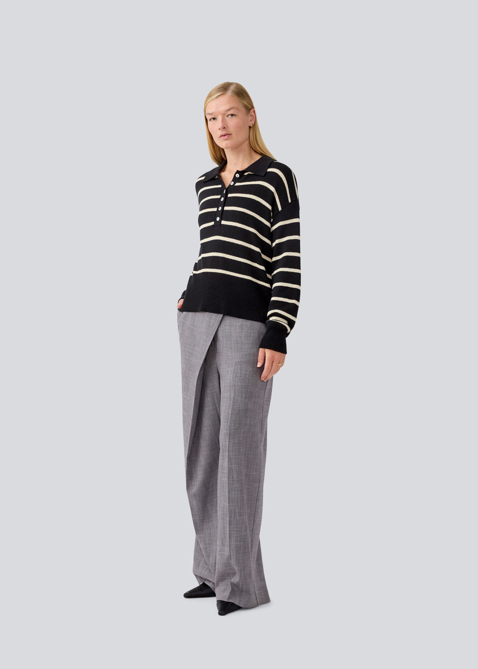 Blød strikket polo i sort med beige striber. MalvaMD stripe polo har en krave med stolpelukning. Modellen er 177 cm og har en str S/36 på. Strikken er lille i størrelsen, og kort.