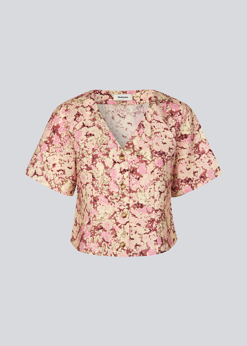 Figursyet top med korte ærmer. MeliaMD print top har en v-hals og knappelukning fortil. Modellen er 177 cm og har en str S/36 på.