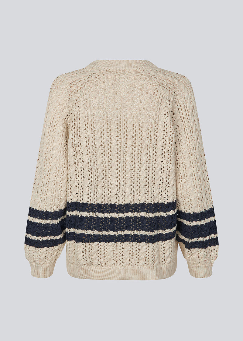 Løs strikket cardigan i beige med mørkeblå striber i kabel strik. MetteMD cardigan er let gennemsigtig, har løse ærmer og en knappelukning fortil. Modellen er 177 cm og har en str. S/36 på.