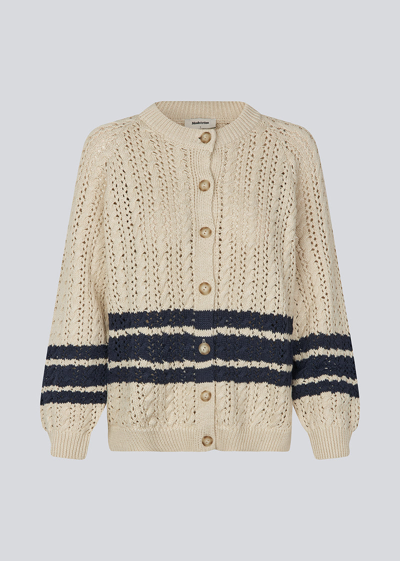 Løs strikket cardigan i beige med mørkeblå striber i kabel strik. MetteMD cardigan er let gennemsigtig, har løse ærmer og en knappelukning fortil. Modellen er 177 cm og har en str. S/36 på.