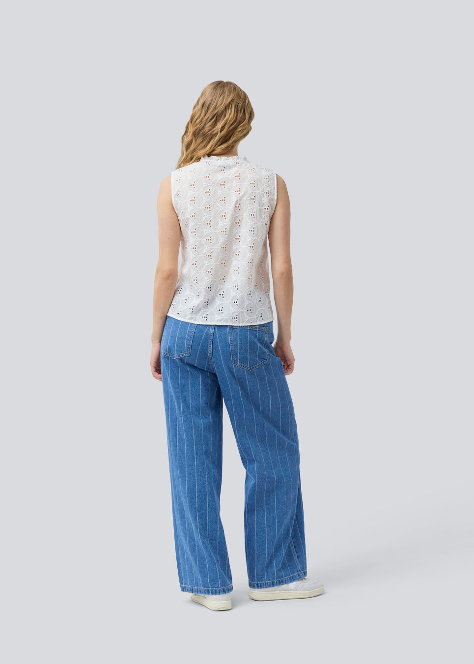 Ærmeløs hvid top i broderie anglaise. NanetteMD top har en høj hals og en knappelukning fortil.