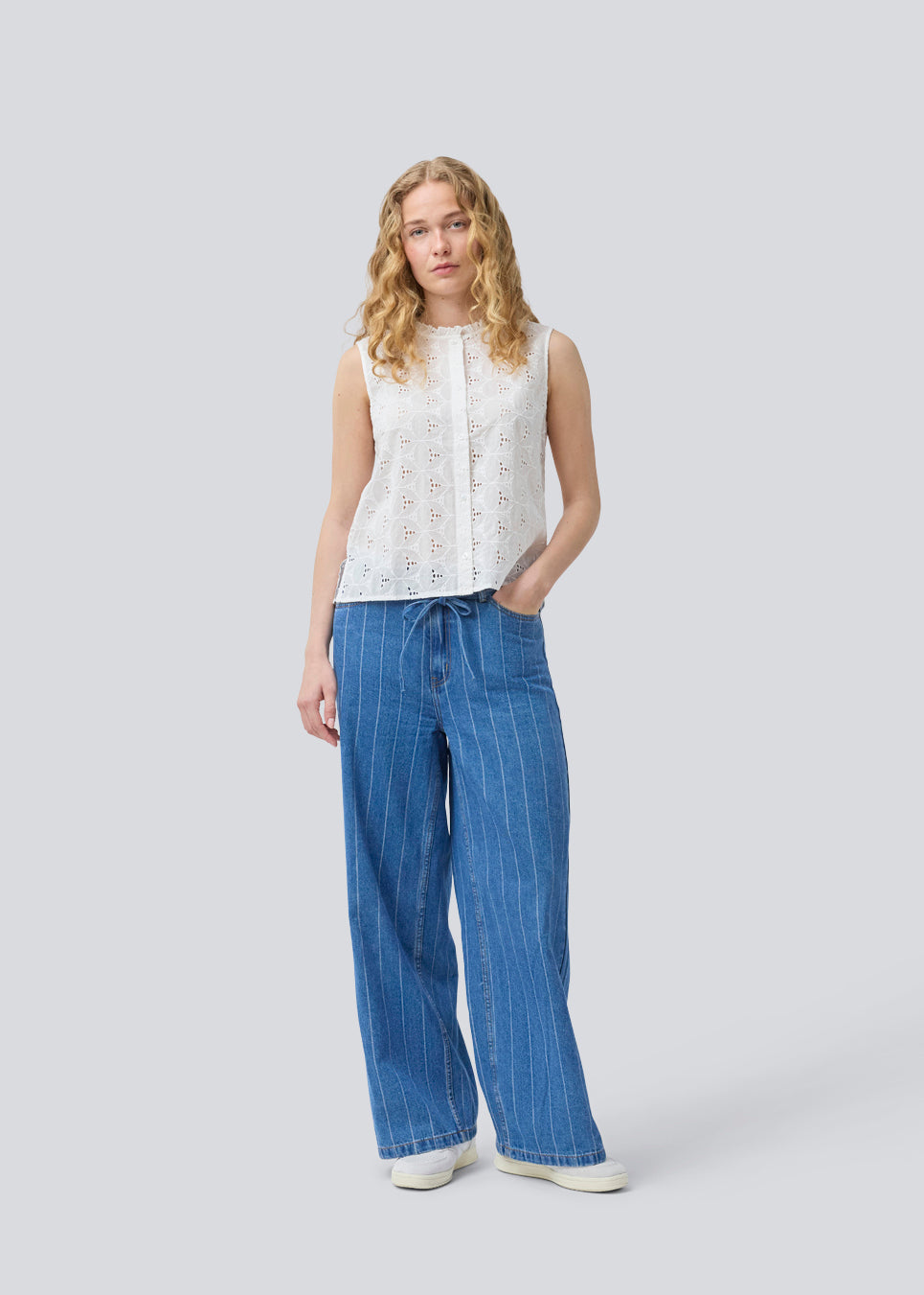 Ærmeløs hvid top i broderie anglaise. NanetteMD top har en høj hals og en knappelukning fortil.