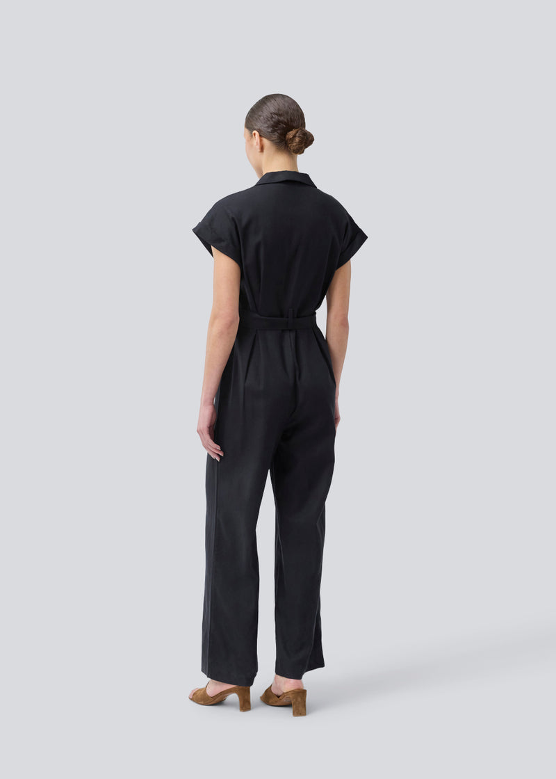 Sort jumpsuit med vidde ben og bindebånd i taljen. NedraMD jumpsuit har en krave, v-hals og lynlåslukning fortil.