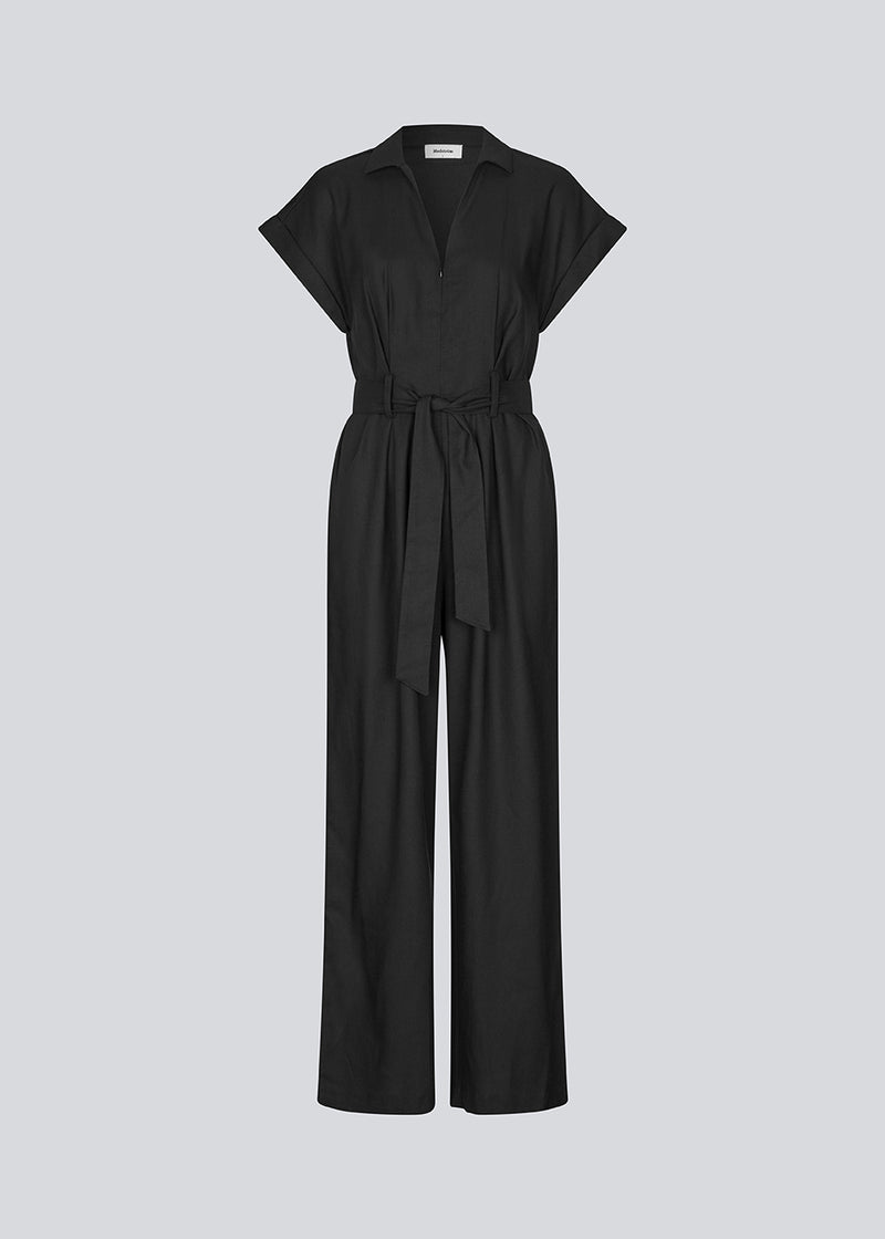 Sort jumpsuit med vidde ben og bindebånd i taljen. NedraMD jumpsuit har en krave, v-hals og lynlåslukning fortil.