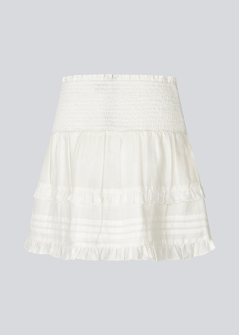 Kort hvid nederdel i 100% økologisk bomuld. NillaMD skirt har et løst skørt med læg og flæsedetaljer og en elastisk talje med smock.