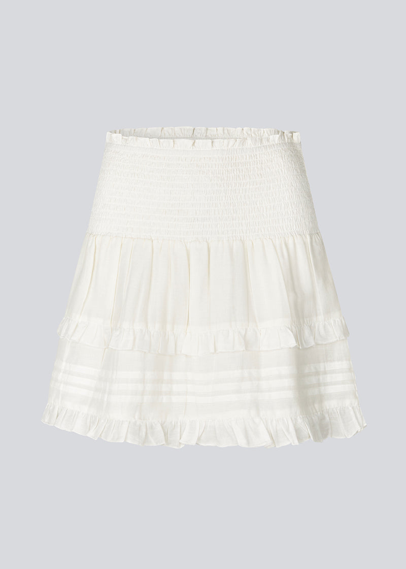 Kort hvid nederdel i 100% økologisk bomuld. NillaMD skirt har et løst skørt med læg og flæsedetaljer og en elastisk talje med smock.