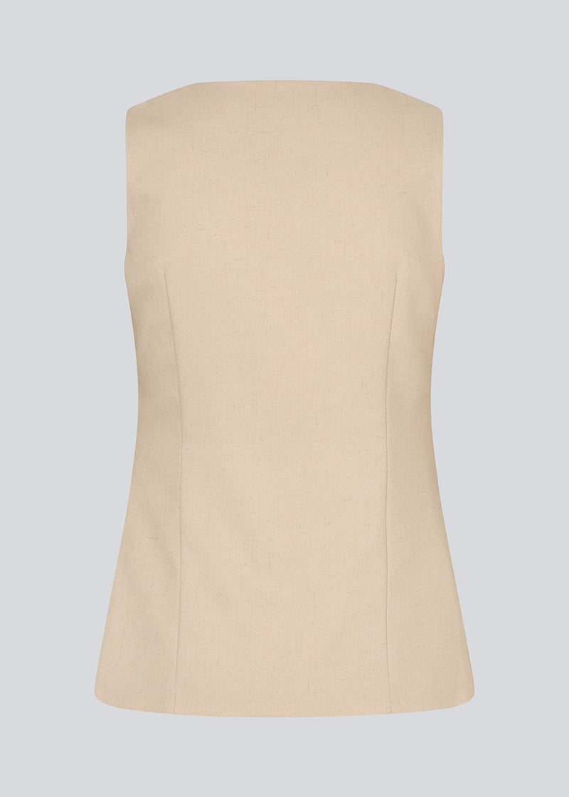 Figursyet beige vest med v-udskæring. NormaMD top har en knappelukning og to lommer fortil.
