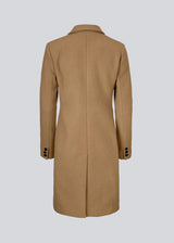 Smuk knælang uldfrakke i lys brun. Odelia coat bliver lukket fortil af fire knapper og er taljeret, hvilket giver et feminint udtryk. På grund af den høje kvalitet af uld, vil den være det oplagte valg til både efterår og de milde vintre.