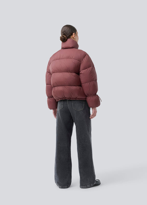 Rød dunjakke med høj hals i 100% genanvendt polyester. Odinmd jacket har en lynlåslukning og en justerbar elastik i ærmet. Modellen er 175 cm og har en str. s/36 på.
